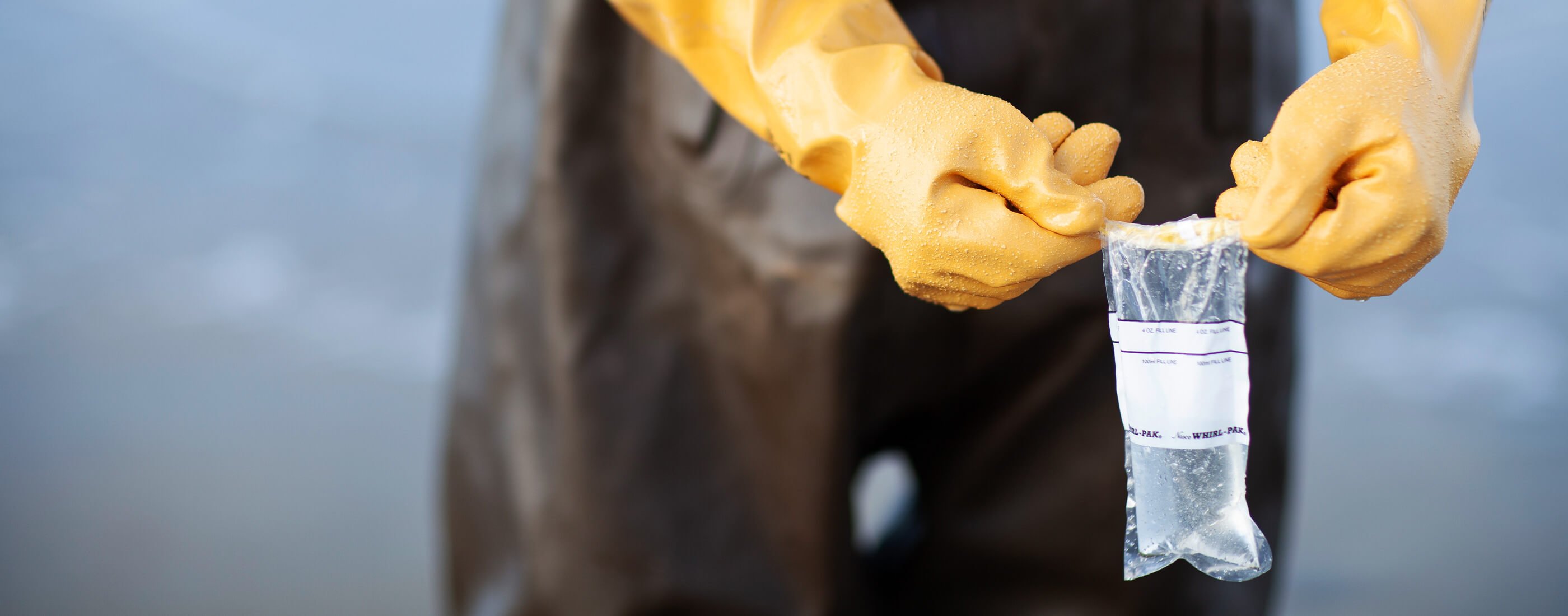 Hands in yellow gloves hold up ocean water sample bag