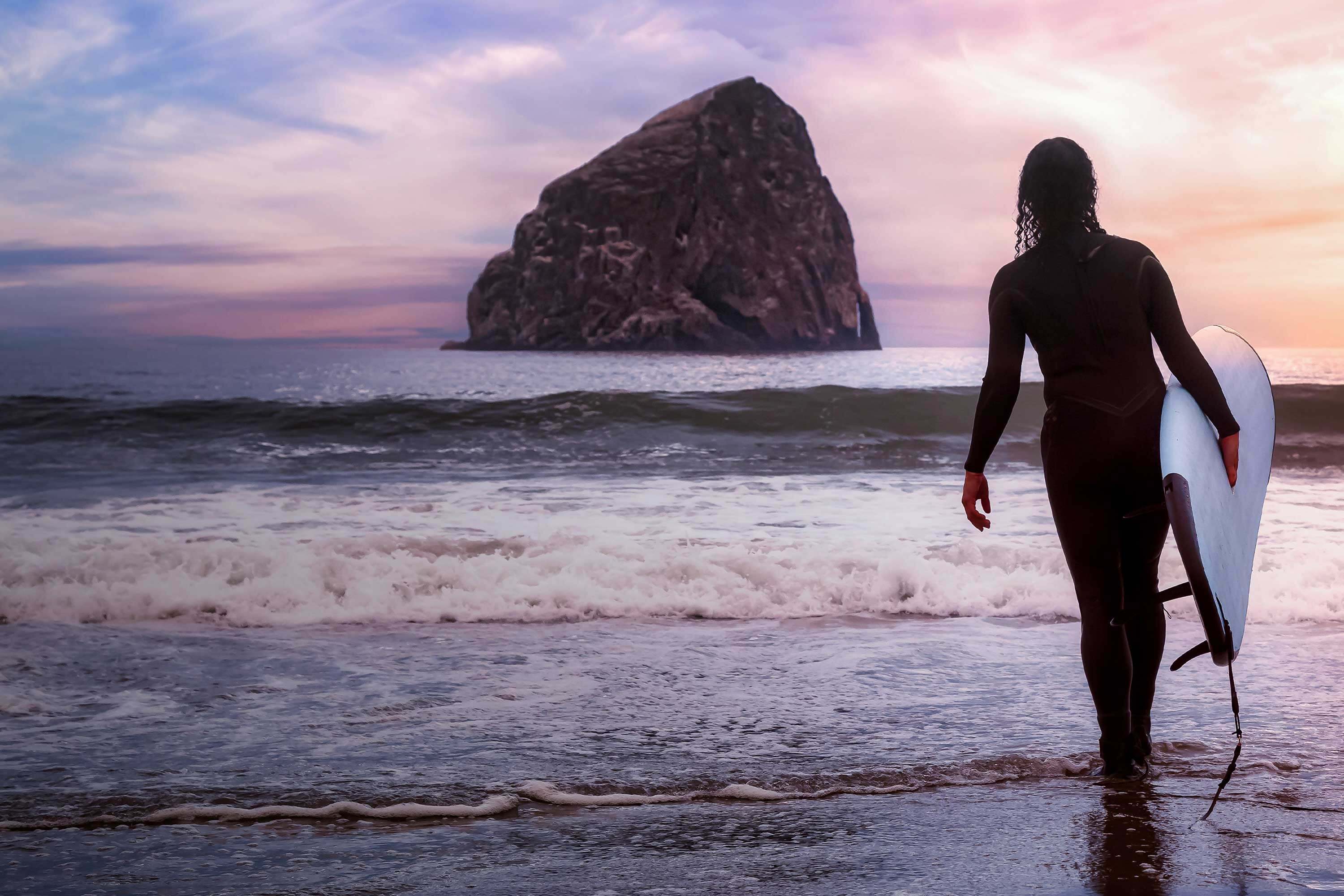 Person with surfboard walks on beach toward water